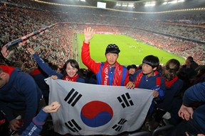 축구장을 뒤로하고 젋은이들이 태극기를 들고 손을 흔들고 있는 사진